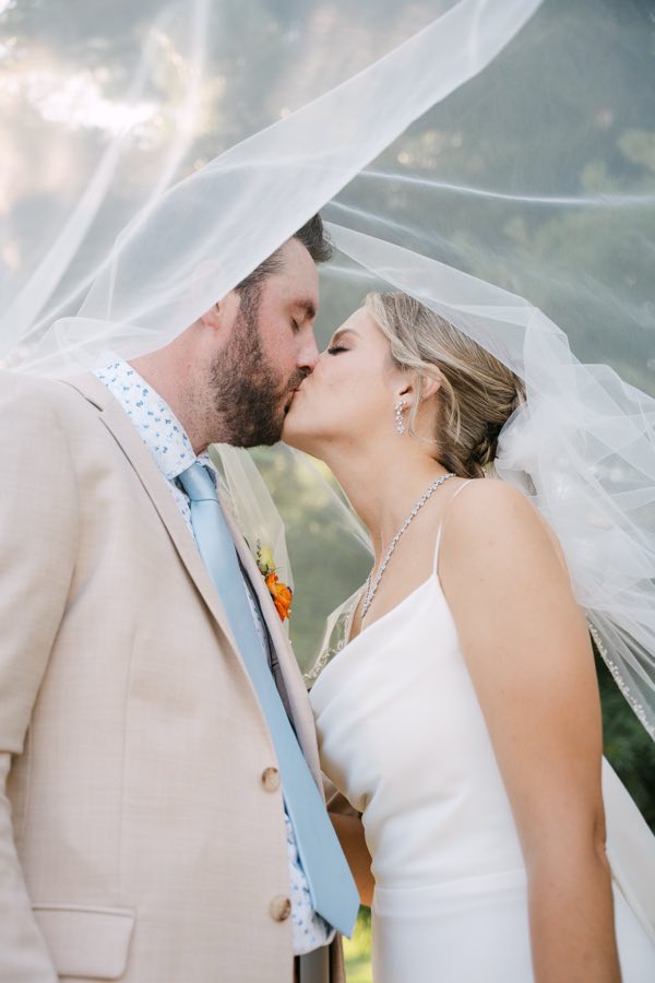 A couple kissing beneath a veil lifted by the wind