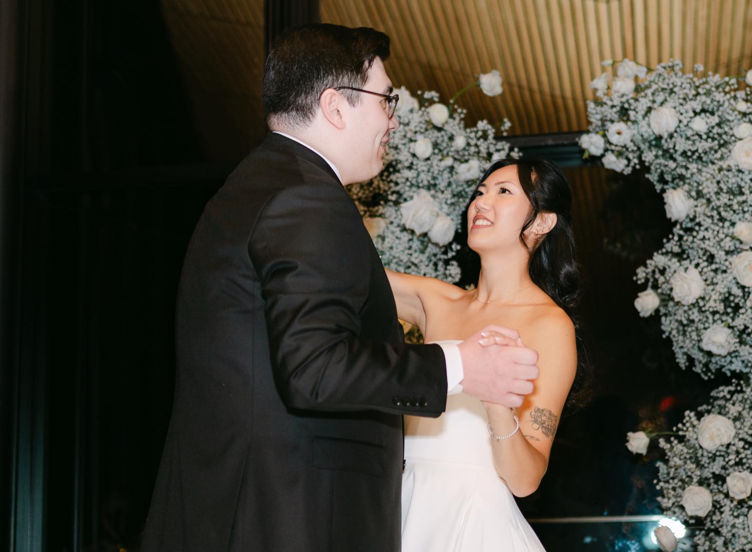 A couple laughing together during their first dance, lit by warm ambient light